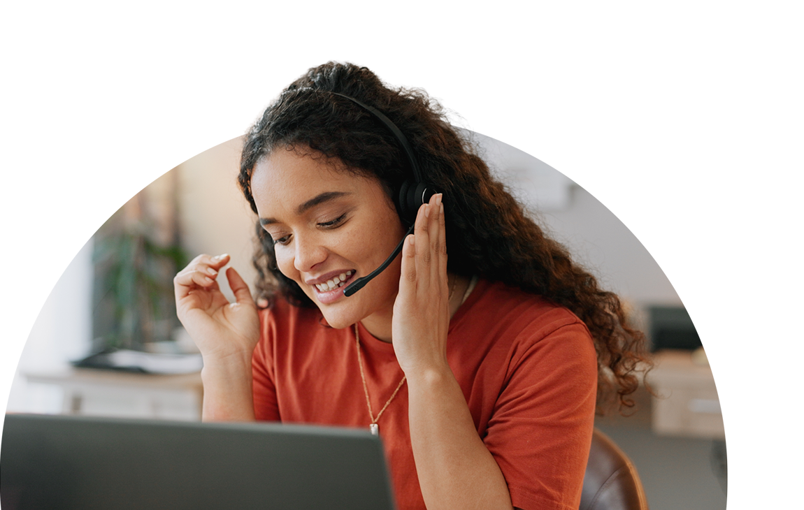 Smiling woman with a headset on, apparently having a conversation with someone on the computer in front of her